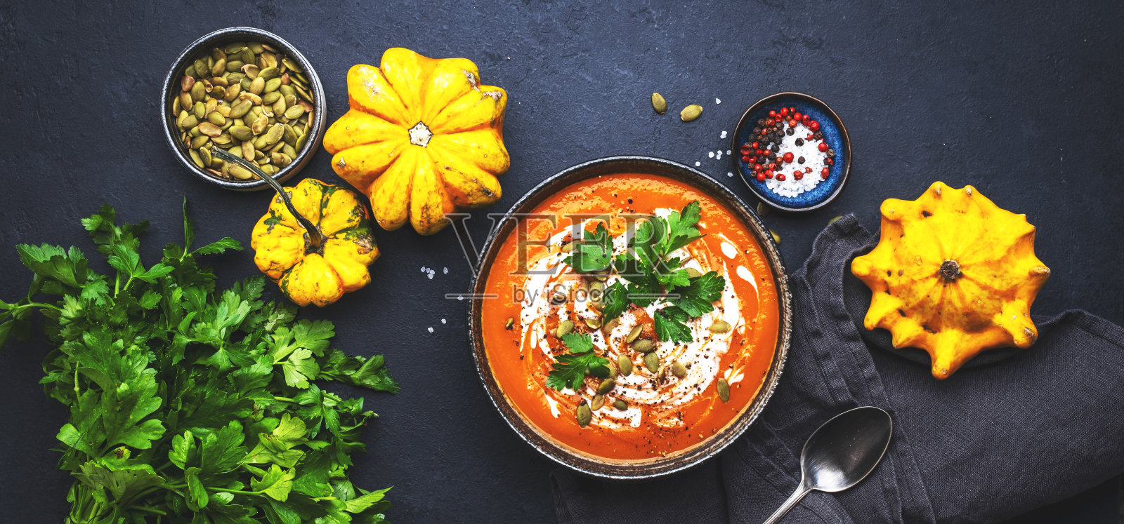 用南瓜子、奶油、胡椒粉和欧芹做成的秋季南瓜汤泥。冬天健康的素食慢的安慰食物。汤碗在黑色的桌子背景。俯视图照片摄影图片