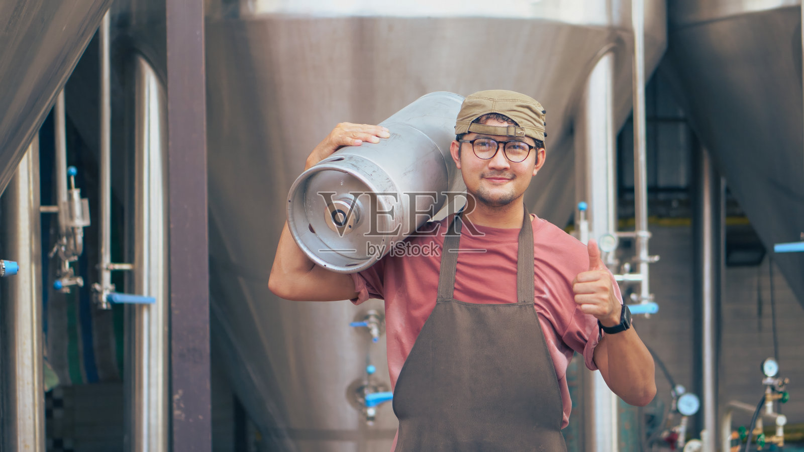亚洲男工人在精酿啤酒厂提桶啤酒。照片摄影图片