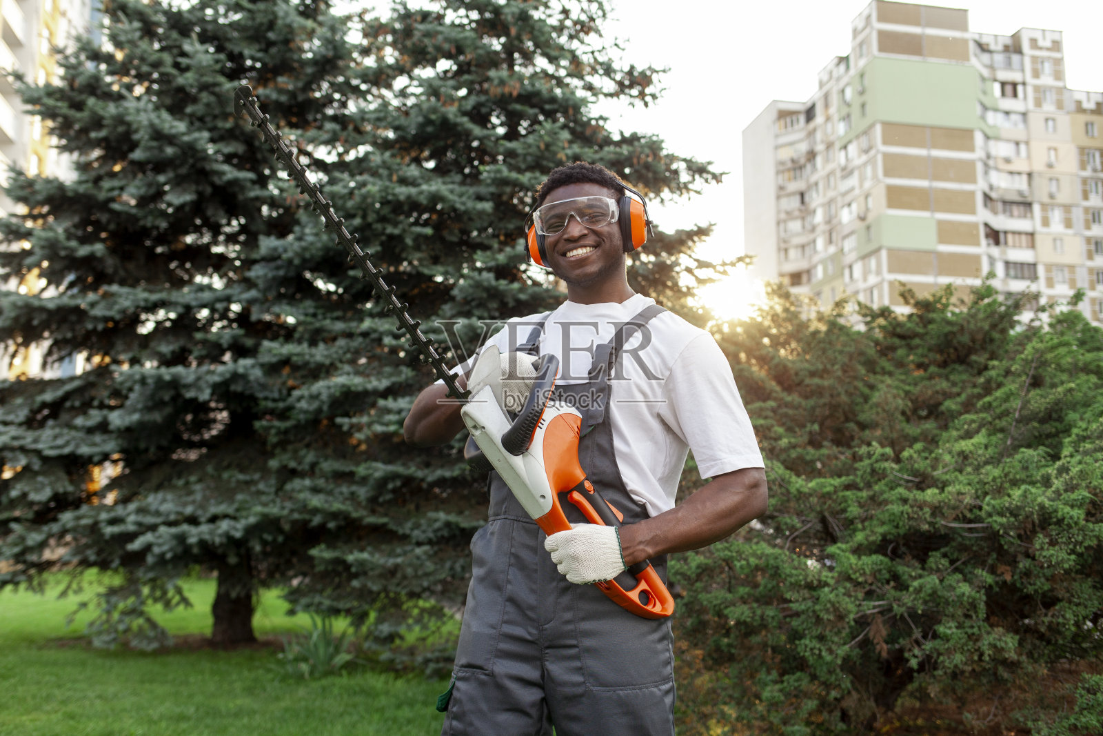 穿着制服的非裔美国男性园艺工人正在用电动工具修剪灌木丛照片摄影图片