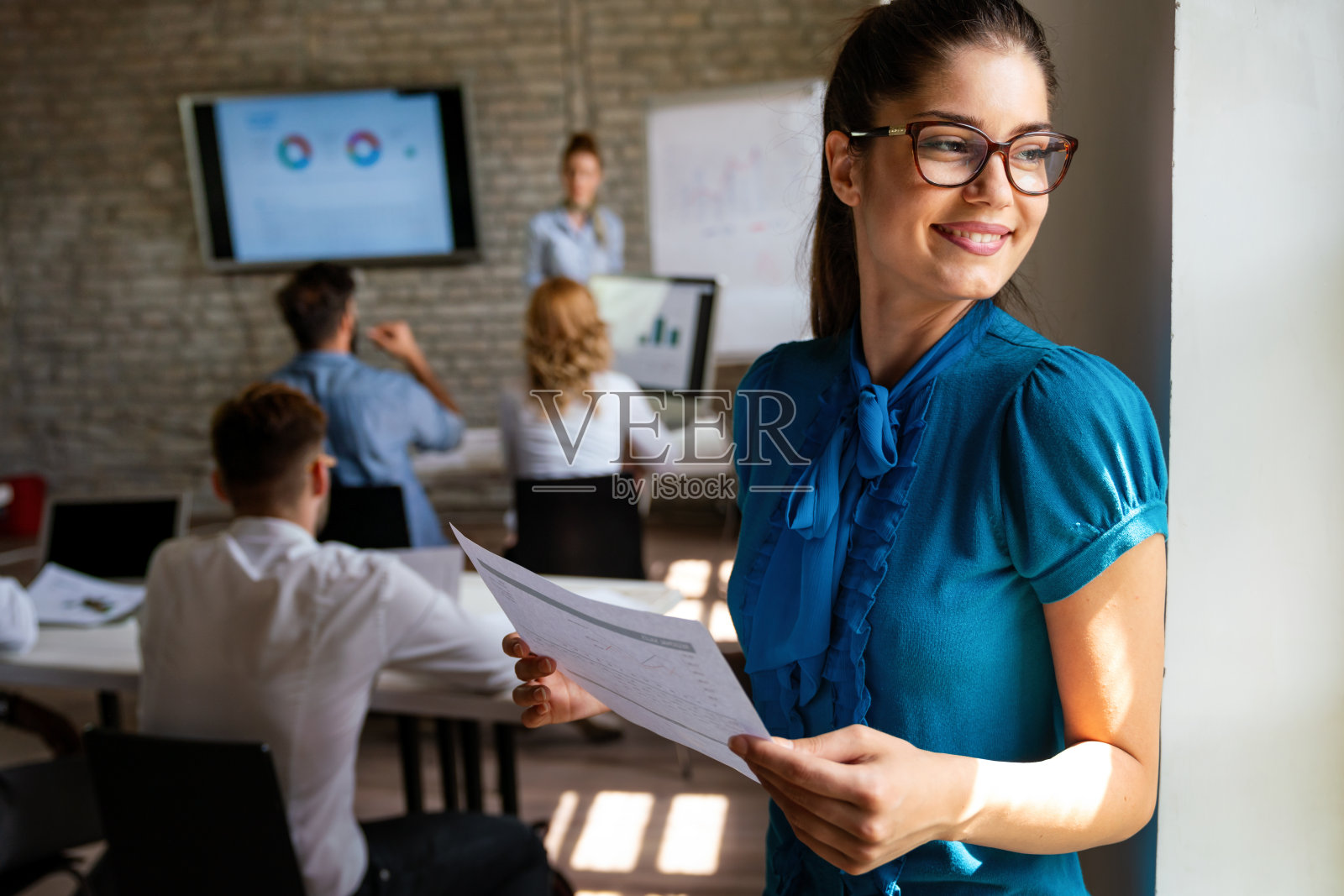 在团队会议上，微笑自信的成功女商业领袖站在办公室里。照片摄影图片