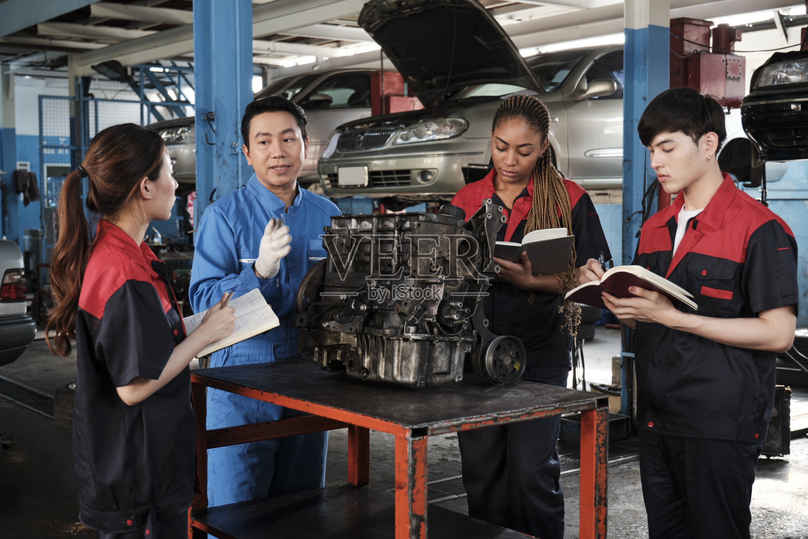 主管工程师正在汽车修理厂教机械工人有关汽车发动机的知识。照片摄影图片