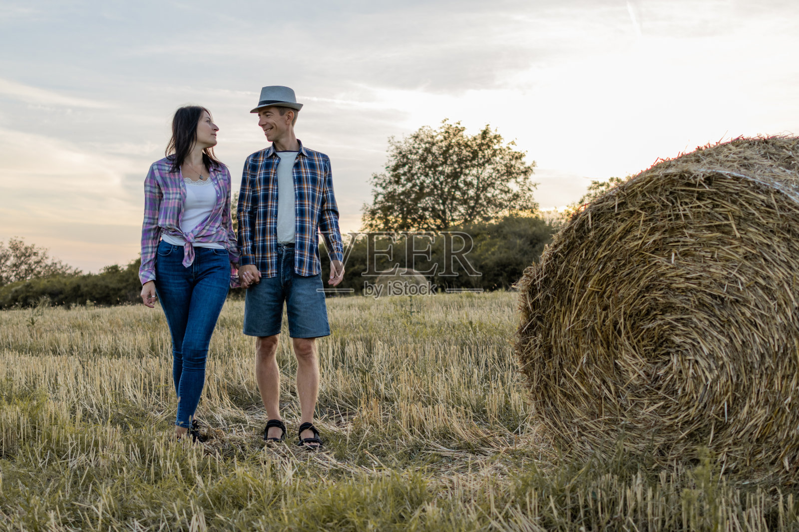 一对幸福浪漫的情侣在美丽的干草地里享受着快乐。他们正在农田里走过夏天收获的干草捆。照片摄影图片