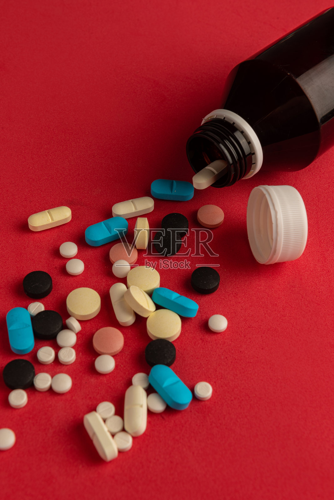 翻倒的药瓶和躺在红色背景上的许多药片。垂直的摄影。副本的空间。药品的概念。照片摄影图片