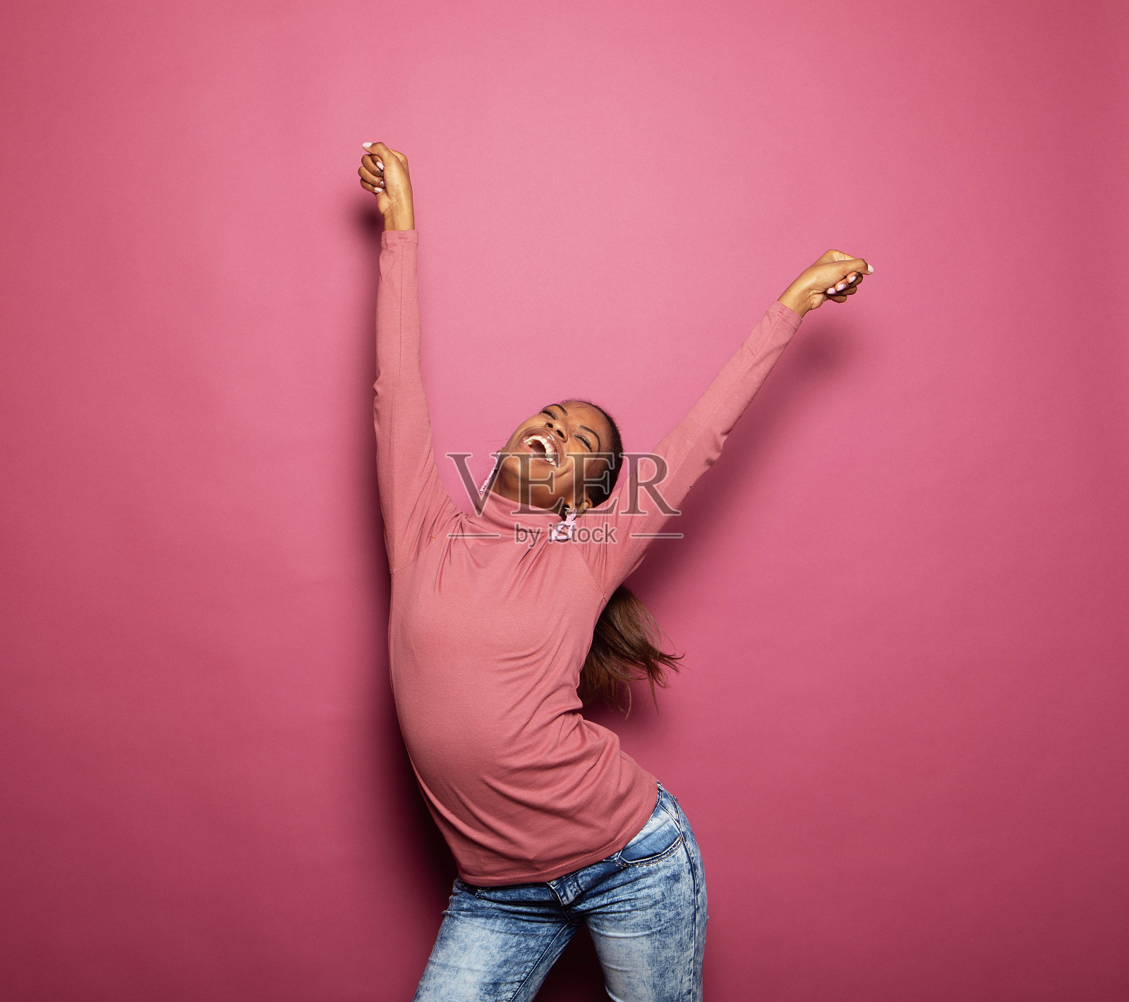 照片中年轻的非洲女子穿着休闲服跳舞，看起来空旷孤立的粉红色背景照片摄影图片