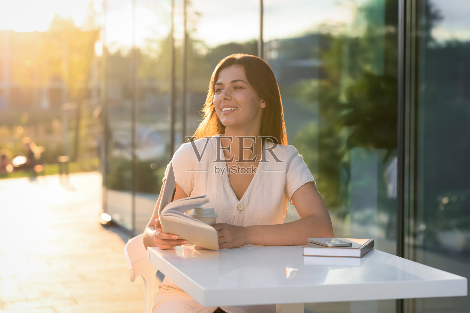 阳光明媚的日子里，年轻女子在户外咖啡馆里拿着咖啡看书照片摄影图片