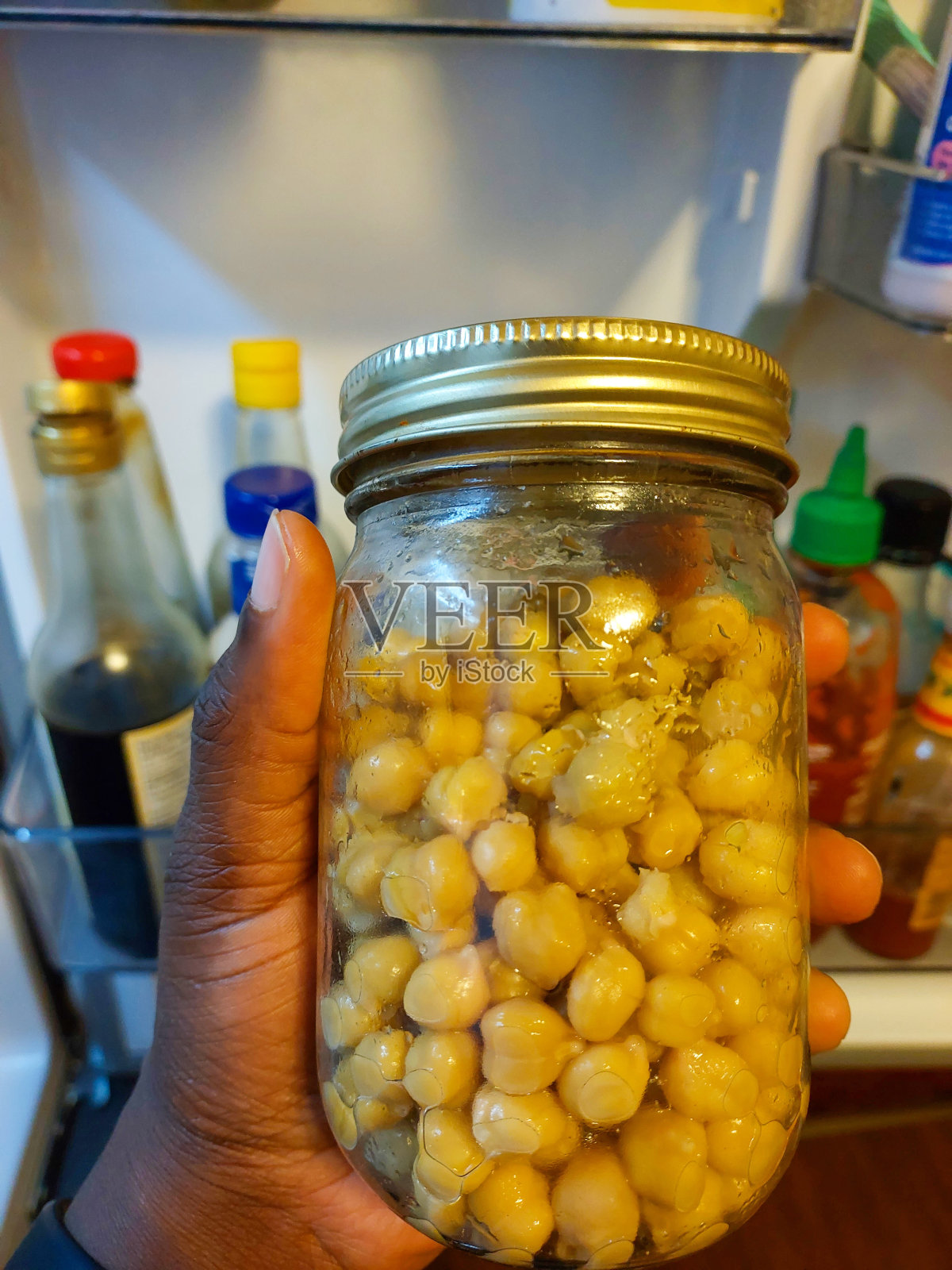 在打开的冰箱前举着一罐鹰嘴豆的人照片摄影图片