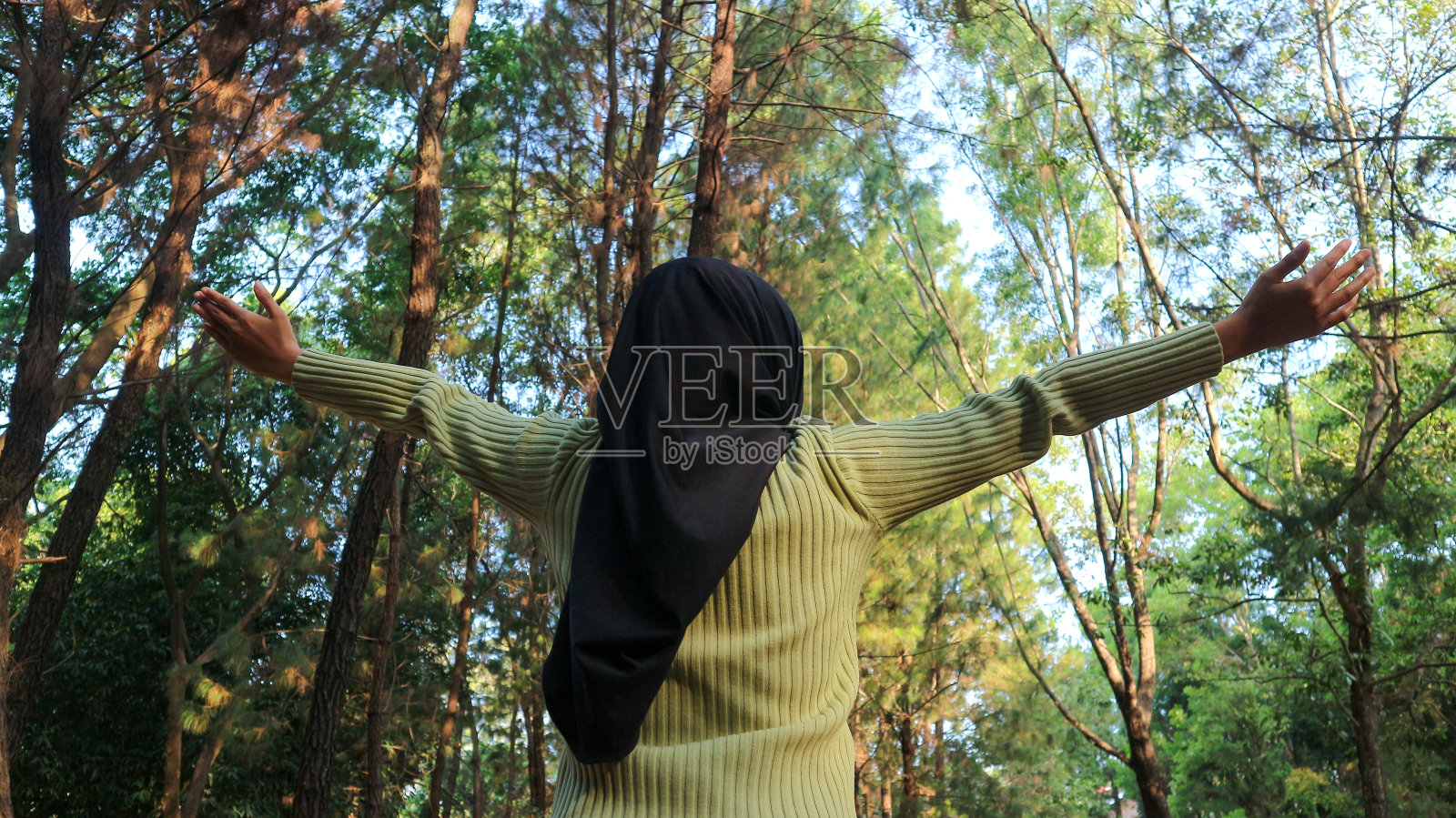 享受大自然。年轻的穆斯林妇女在夏日的绿色公园里高举双臂，享受着新鲜的空气照片摄影图片