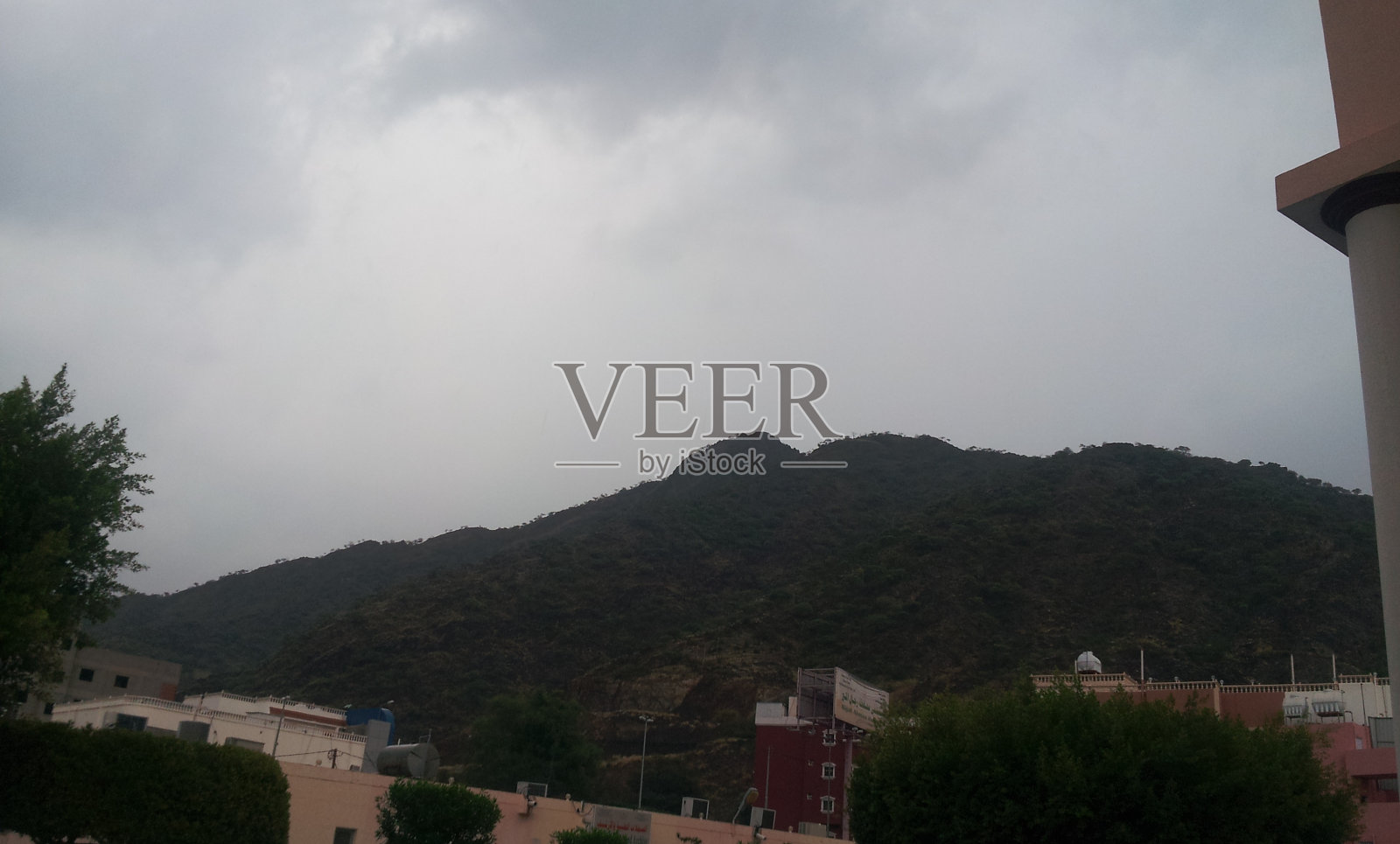 沙特阿拉伯，阿卜哈，通往Rijal Al Maa市的入口道路，周围是住宅建筑，背景是树木和山脉，天空中有云照片摄影图片