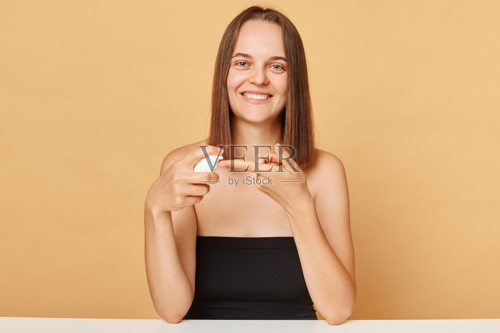 微笑开朗满意的妇女拿着洗面奶前，尝试新的护肤产品隔离在米色背景享受美容治疗程序。照片摄影图片