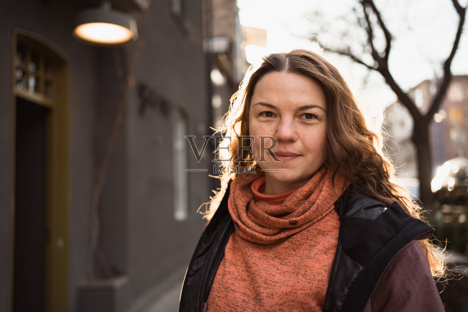 阳光明媚的日子里，穿着冬衣的女人微笑着走在城市里照片摄影图片