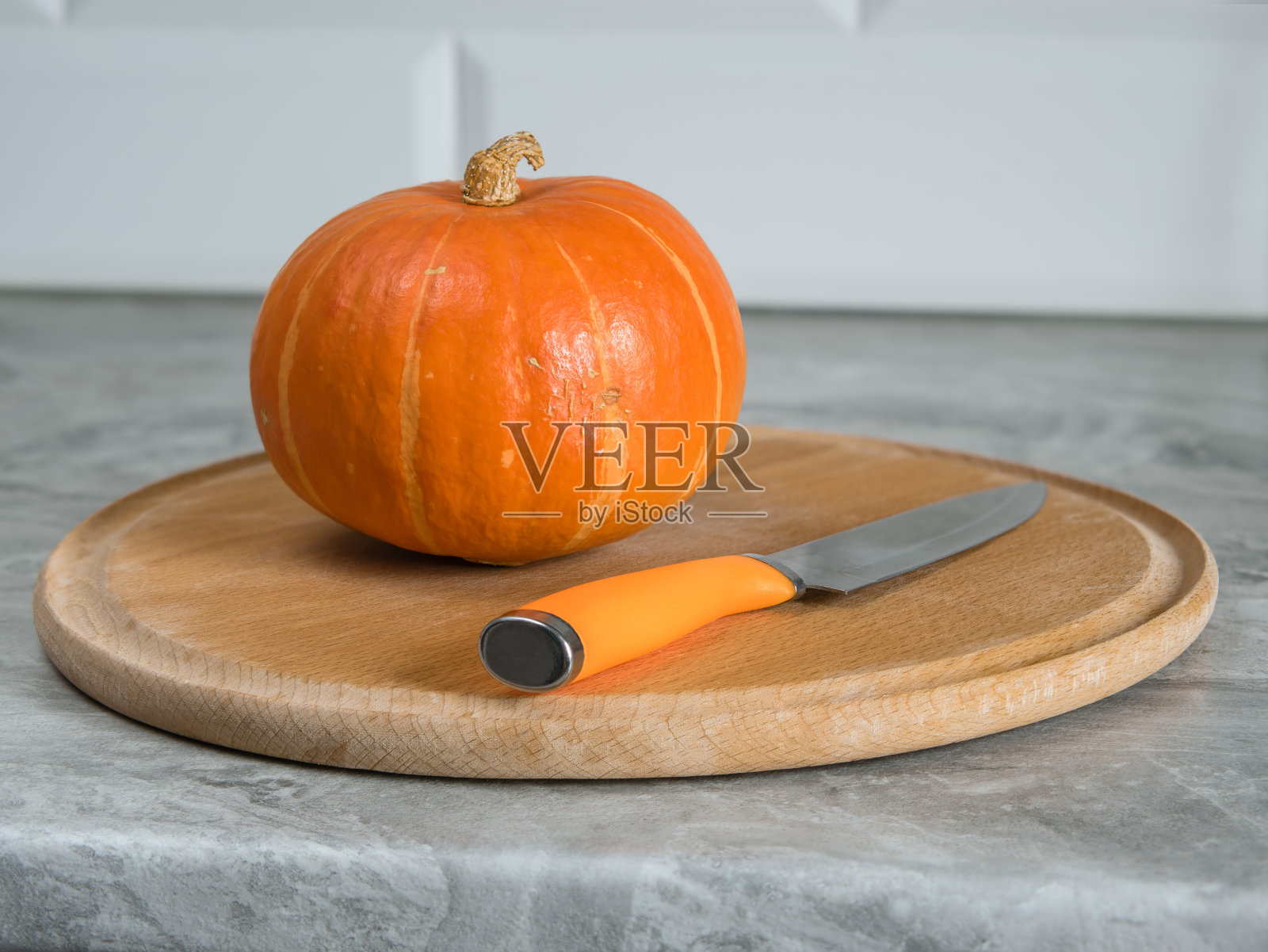 南瓜放在一个圆形的山毛榉砧板和一把橙色手柄的刀上照片摄影图片