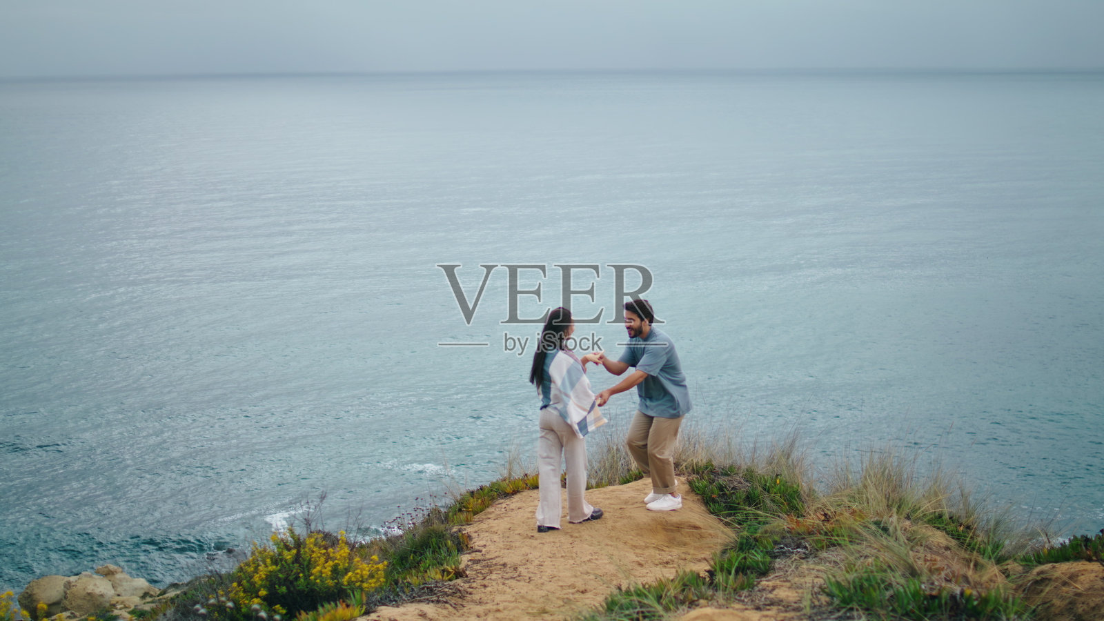 滑稽的夫妇跳舞的海边山丘多云的晚上。两人在海边拥抱。照片摄影图片