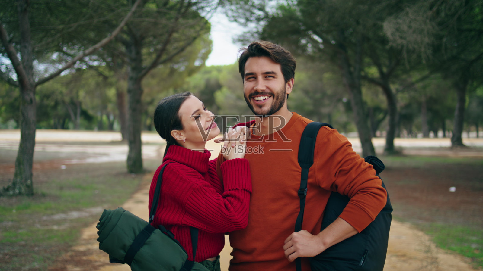 可爱的夫妇背着背包站在森林小路上。女人亲吻男人。照片摄影图片