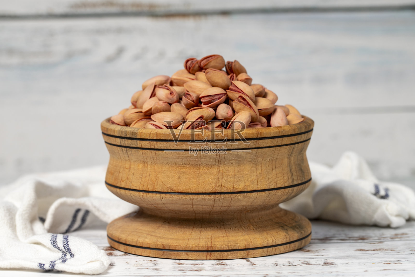 木碗里装着开心果。白色木材背景上的开心果照片摄影图片