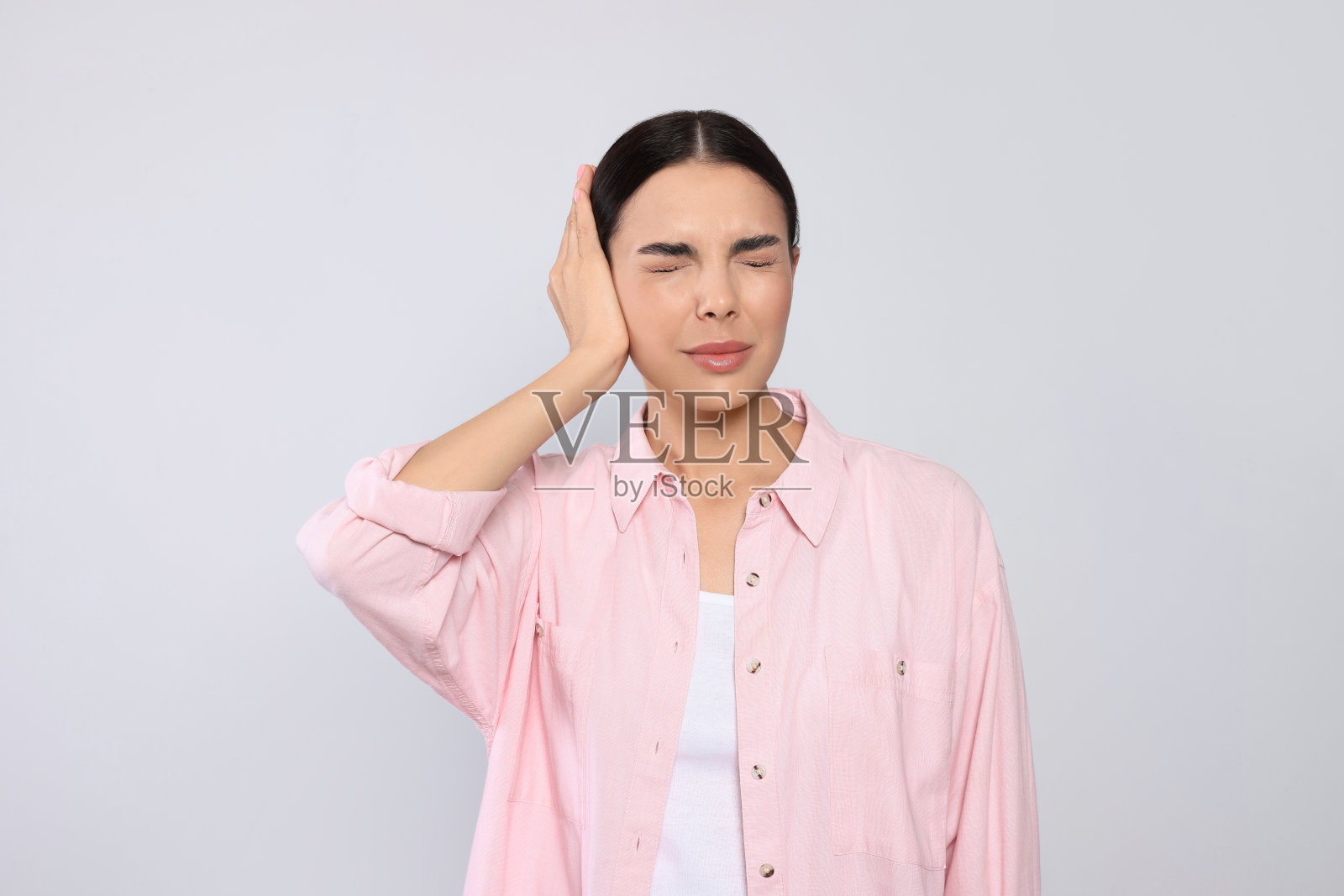 浅灰色背景上患耳痛的年轻女子照片摄影图片