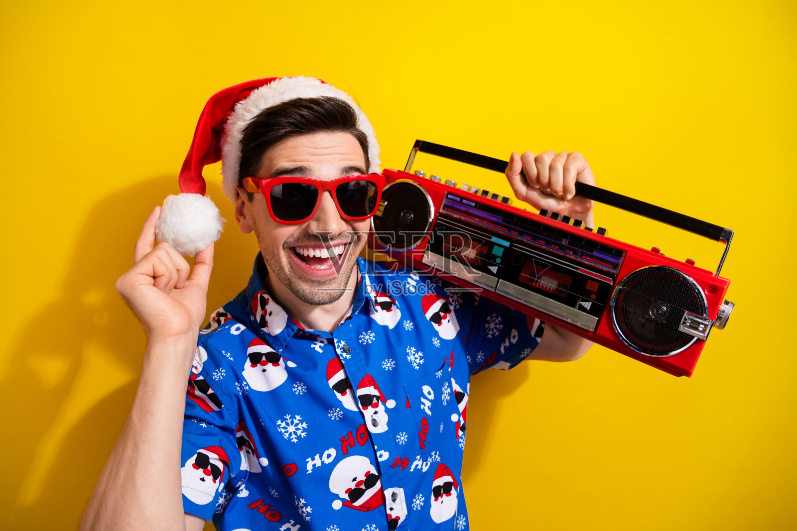 积极兴奋的男人的肖像，带着牙齿微笑，拿着音箱，手臂触摸，拿着头饰，在黄色的背景上孤立的绒球照片摄影图片