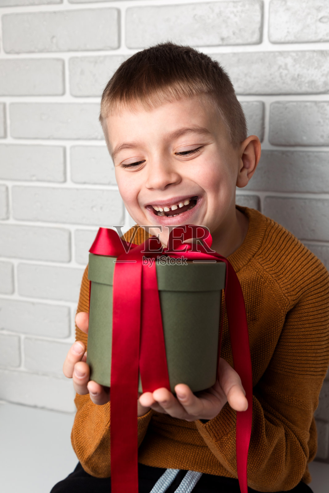 穿着黄色毛衣的漂亮男孩拿着一件用红丝带系着的绿色圆形礼物照片摄影图片