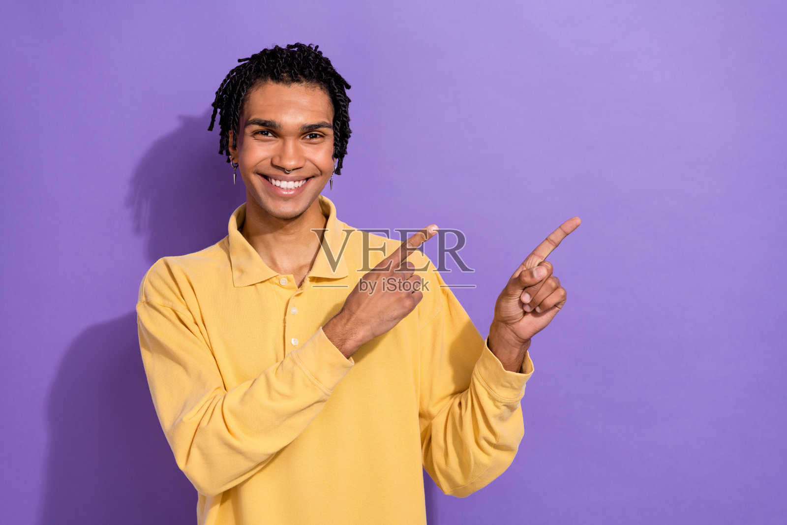 好男人的肖像，戴着时髦的耳环，穿着黄色t恤，在紫色背景上孤立的空间照片摄影图片