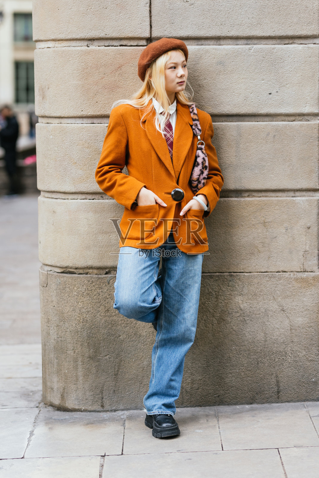 时尚的亚洲女人靠在墙上，双手插在口袋里。照片摄影图片