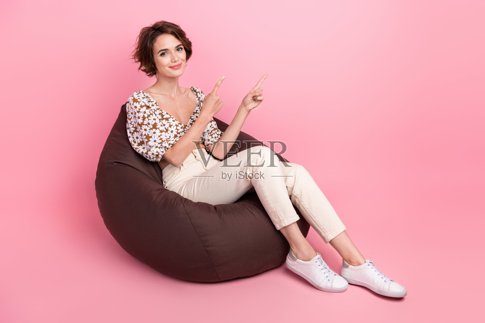 全长照片的积极妇女穿印花顶坐在豆袋表明，在销售空间孤立的粉红色背景照片摄影图片