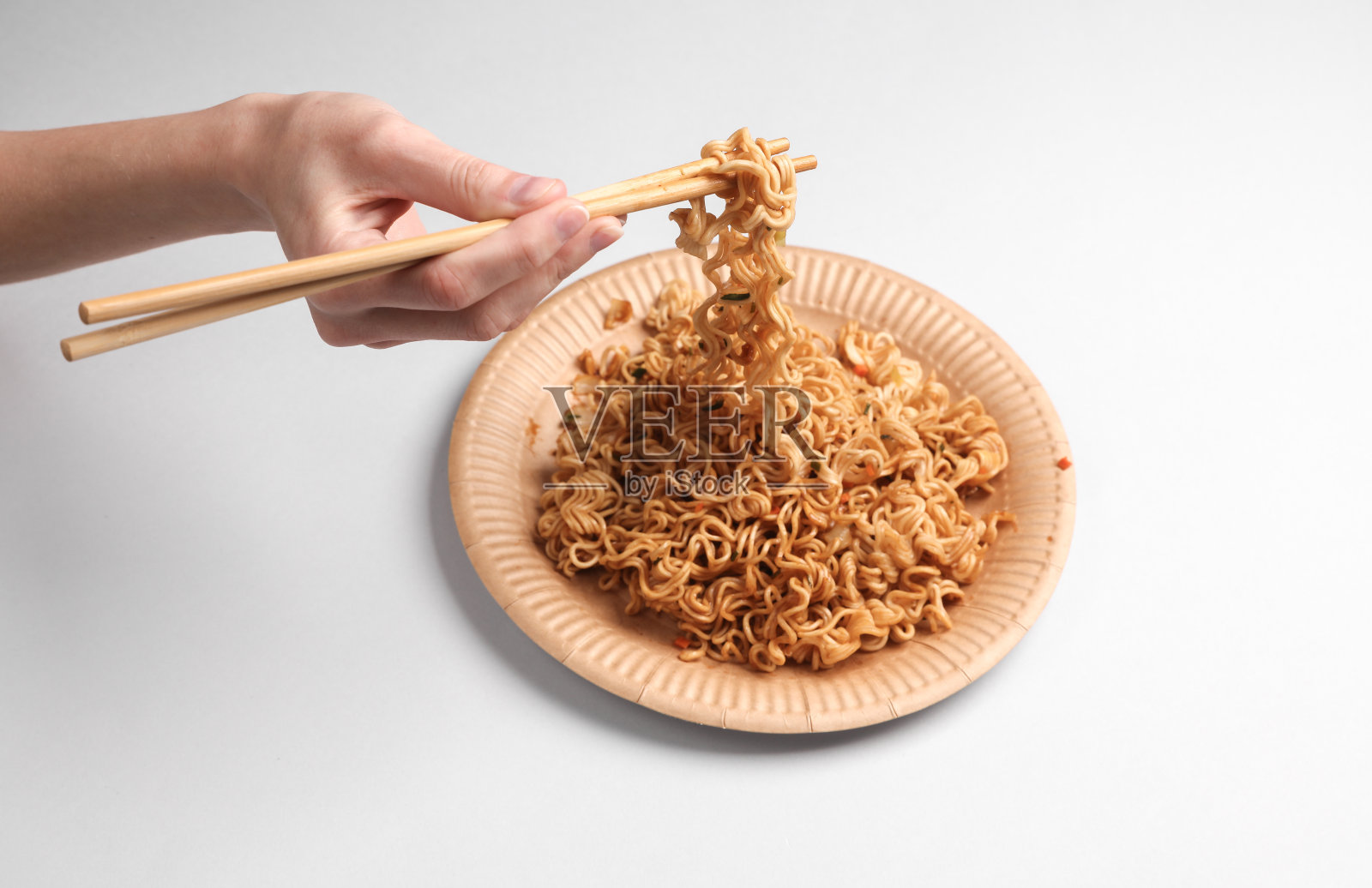 在灰色背景的盘子里，手拿着中国棒子和方便面照片摄影图片