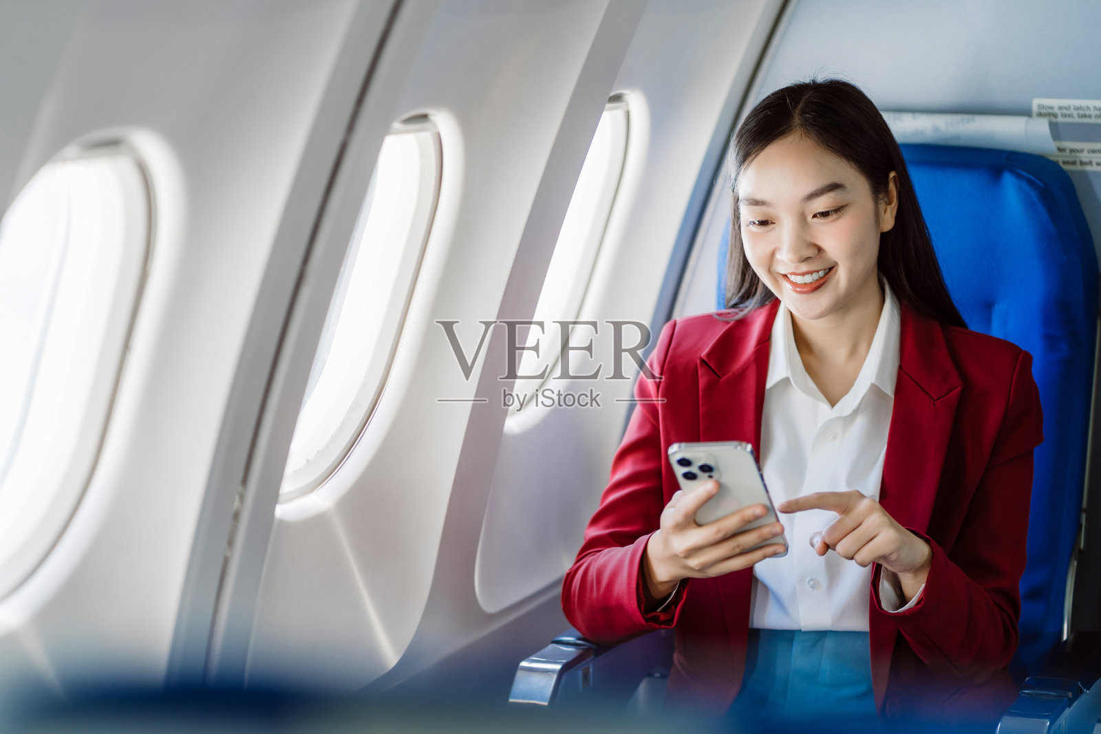 亚洲女游客坐在飞机座位上用上网本查看智能手机通知，年轻的女商人在飞机上用笔记本电脑分享手机上的媒体。照片摄影图片