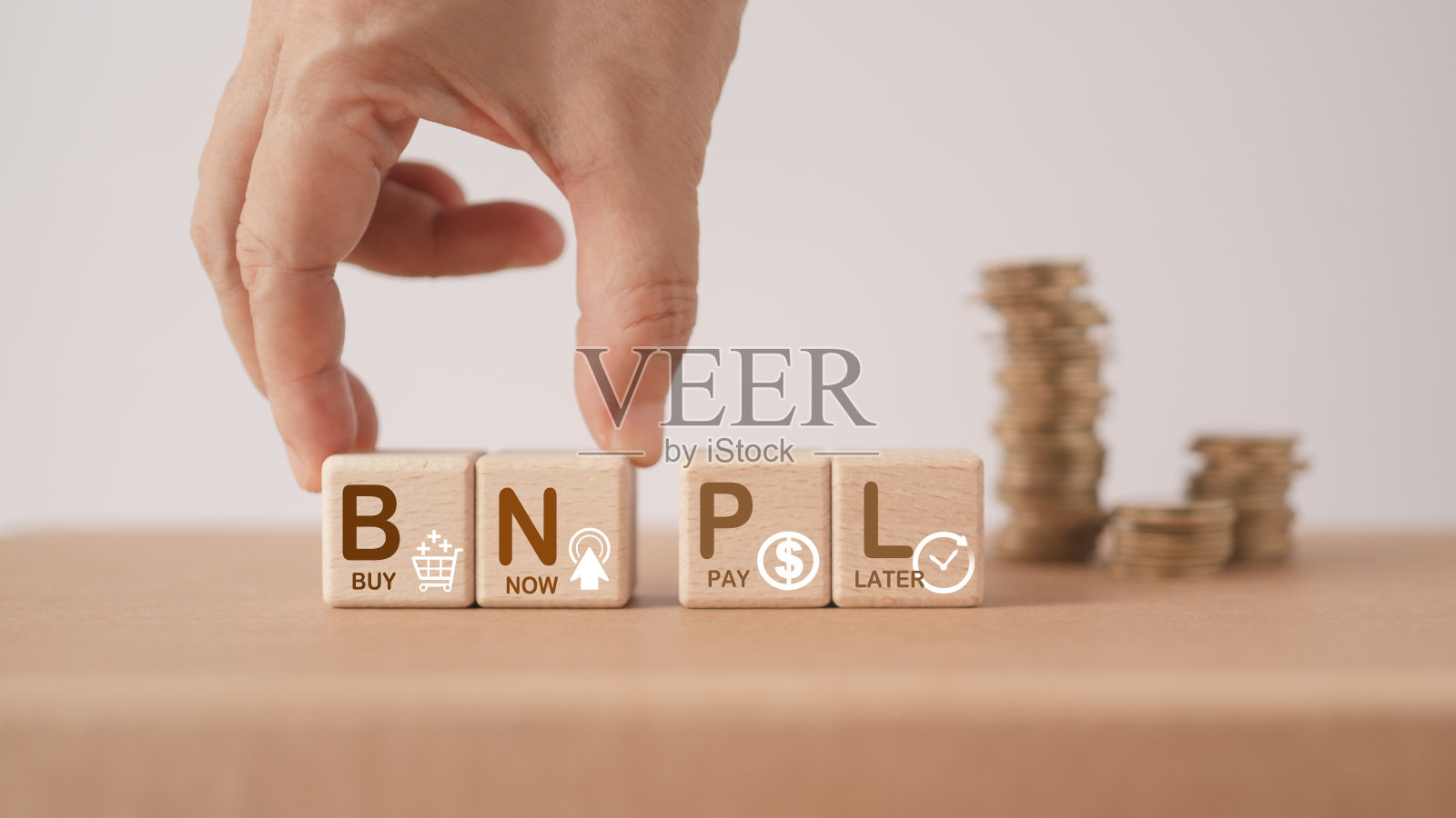 手安排木质立方体块与BNPL，字母缩写，和图标与模糊的硬币堆栈。为现买后付的网上购物理念照片摄影图片