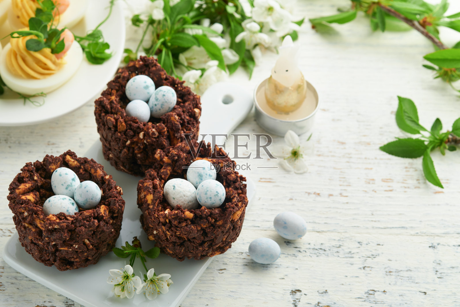 复活节早午餐或早餐。复活节巧克力窝蛋糕有巧克力糖蛋，传统的热十字面包和魔鬼蛋，还有盛开的苹果树花束。春天复活节的节日食品概念。照片摄影图片