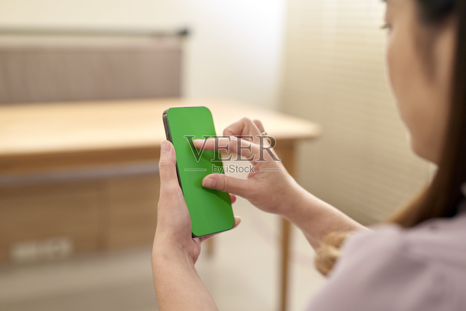坐在家里用绿屏智能手机的女人。照片摄影图片