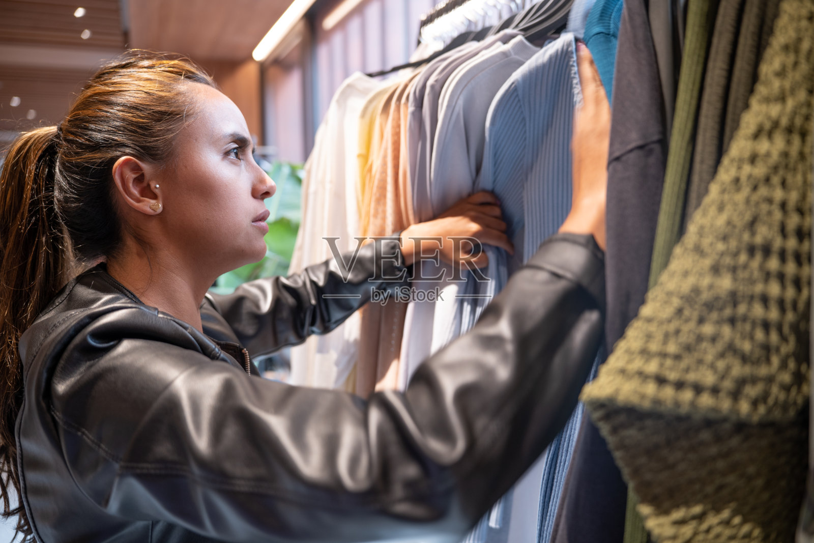 一位美丽的年轻女子在一家现代服装店寻找新衣服，微笑着，专注地看着照片摄影图片
