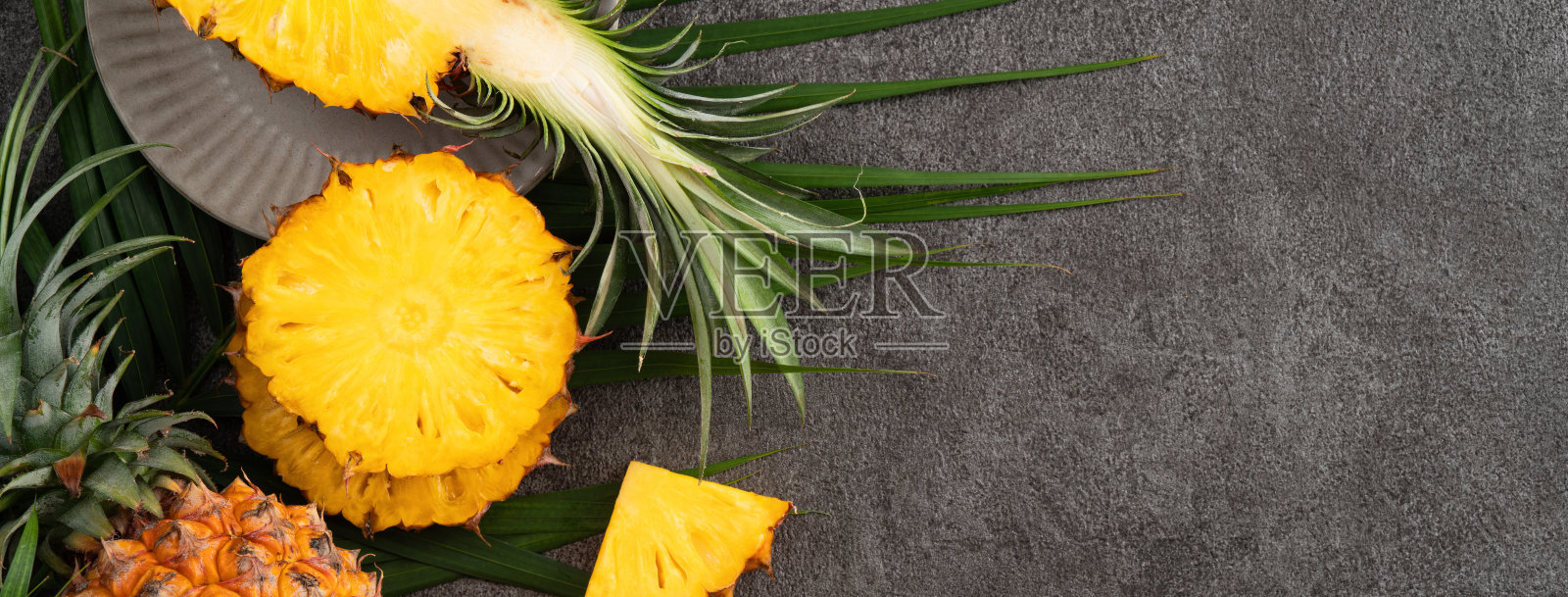 新鲜切菠萝与热带树叶在灰色的桌子背景。照片摄影图片