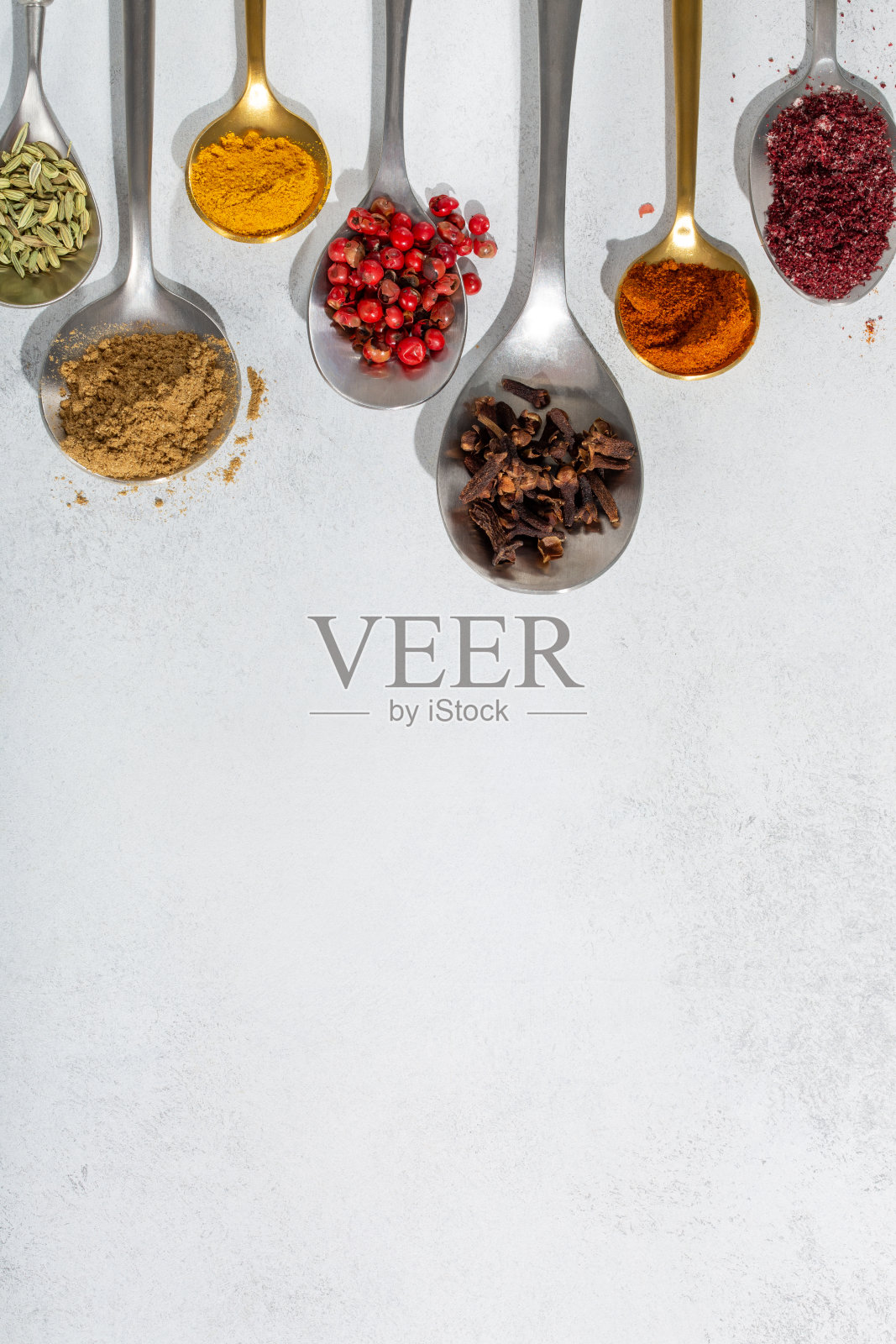 在灰色的背景上，勺子里装着各色香料。食品的背景。俯视图，复制空间。照片摄影图片