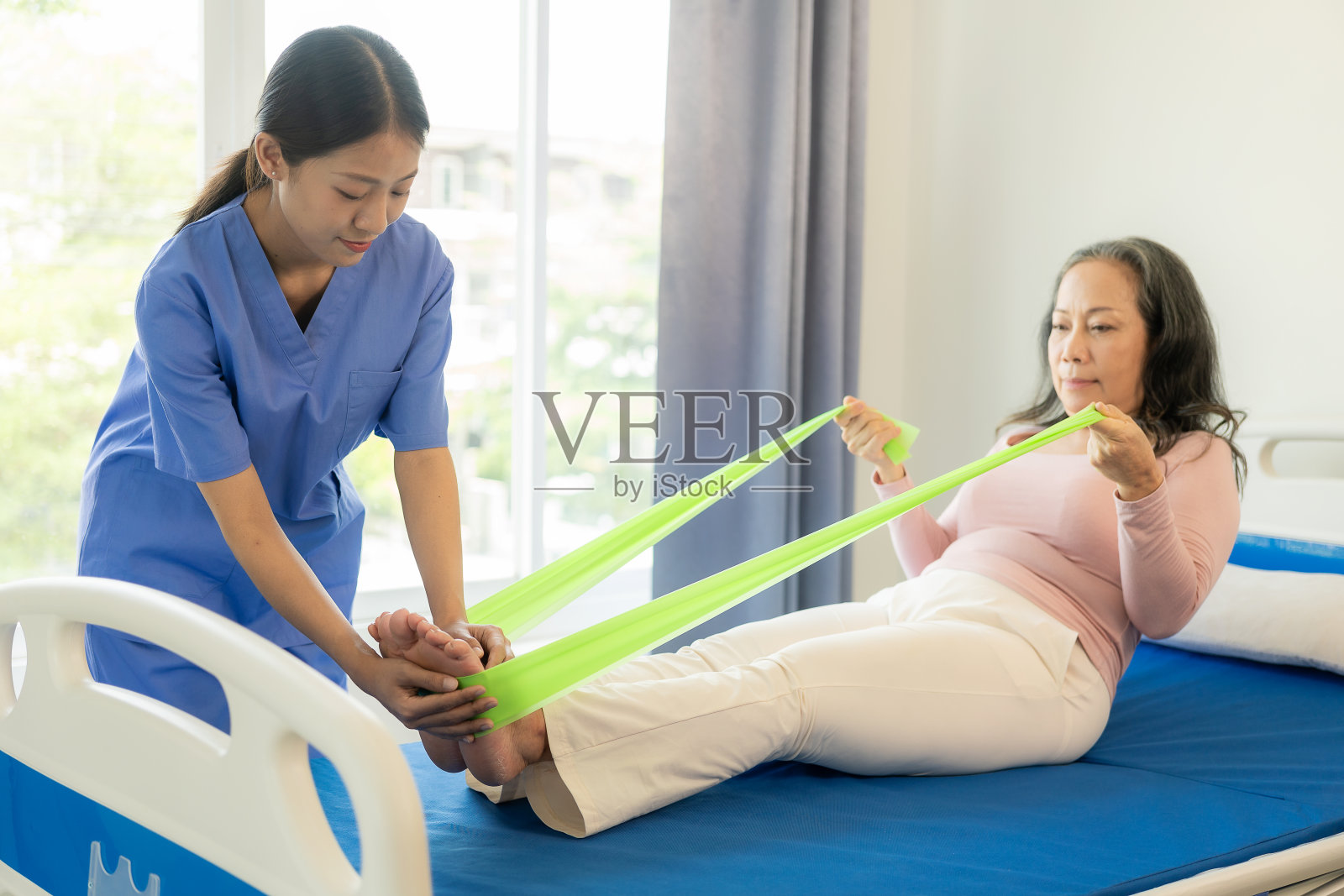 老年女性患者，亚洲女性理疗师扶着她的手臂进行理疗。在医院的检查室里，病人似乎有意做这个练习照片摄影图片