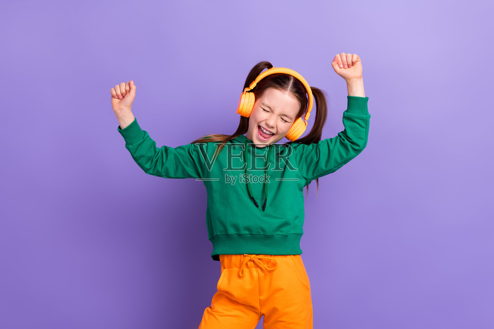 照片的快乐幸运的小女孩穿着绿色连帽衫享受音乐有乐趣孤立的紫色背景照片摄影图片