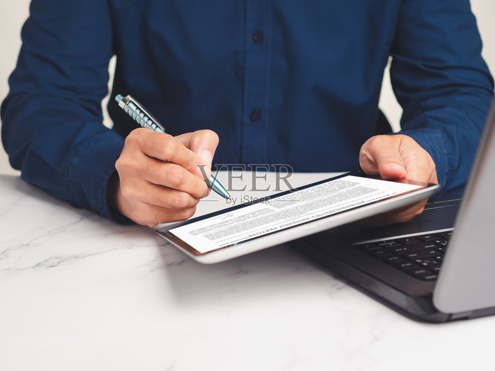 商人坐在办公室的桌子前，在平板电脑上签署数字合同或协议照片摄影图片