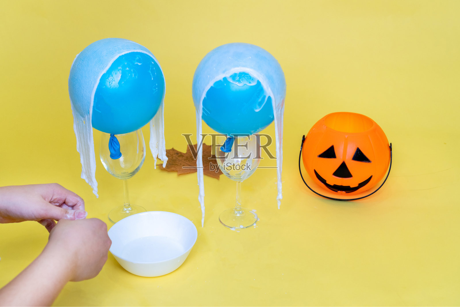 万圣节鬼魂是用绷带、胶水、水、气球和眼镜在黄橙色的背景上做成的。儿童艺术项目。DIY的概念。万圣节的节日概念。5.循序渐进。照片摄影图片