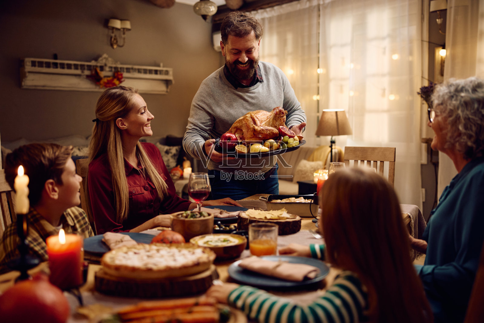 一个快乐的男人在和他的大家庭一起吃感恩节晚餐时，把烤火鸡端到餐桌上。照片摄影图片