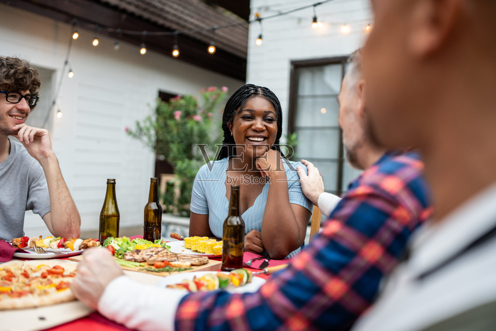 多民族家庭欢聚一堂，在花园享受户外聚会。吸引人的形形色色的人群共进晚餐，吃着美食，欢度周末团聚相聚在餐桌旁。照片摄影图片