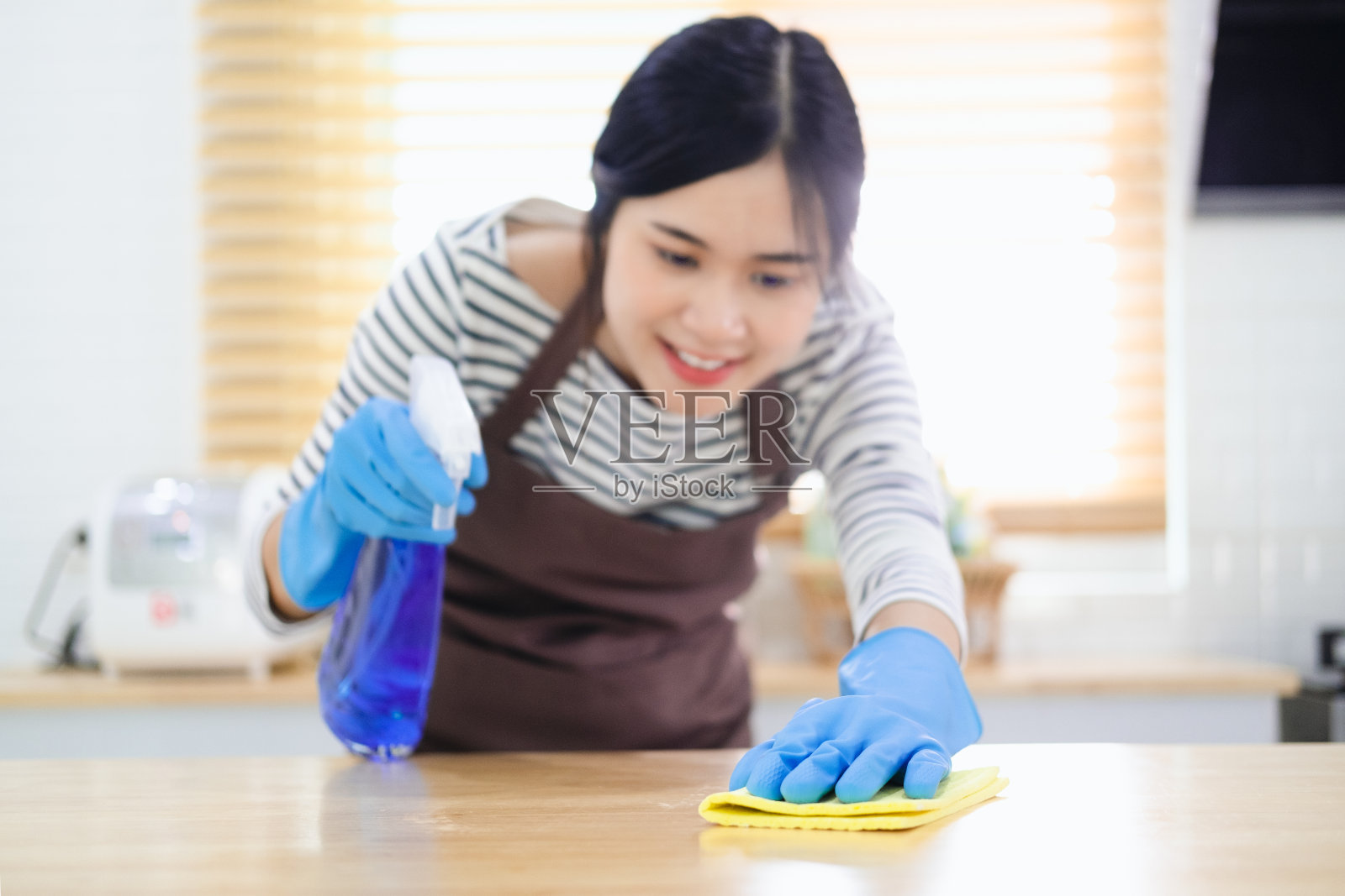 戴着防护手套的妇女微笑着用喷雾器和掸子擦拭灰尘，同时打扫她的房子(特写)照片摄影图片