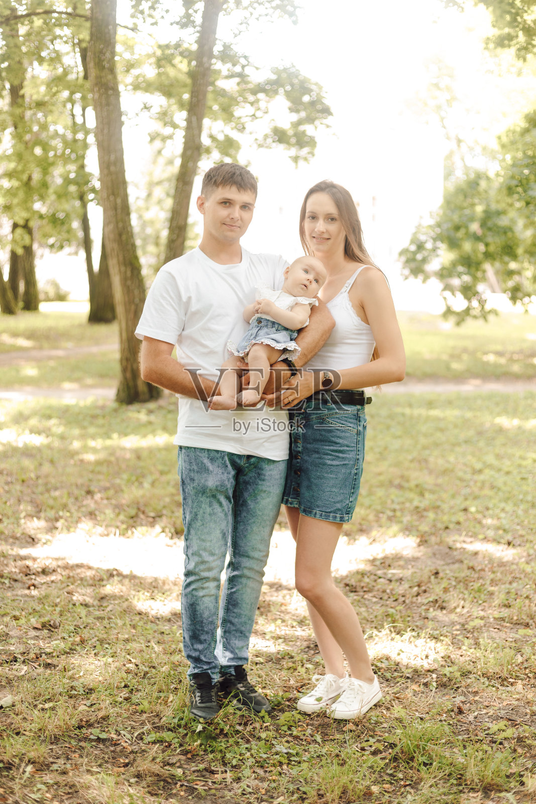 垂直全身像的年轻幸福的家庭。一天，爸爸妈妈和刚出生的婴儿在公园里摆姿势。照片摄影图片