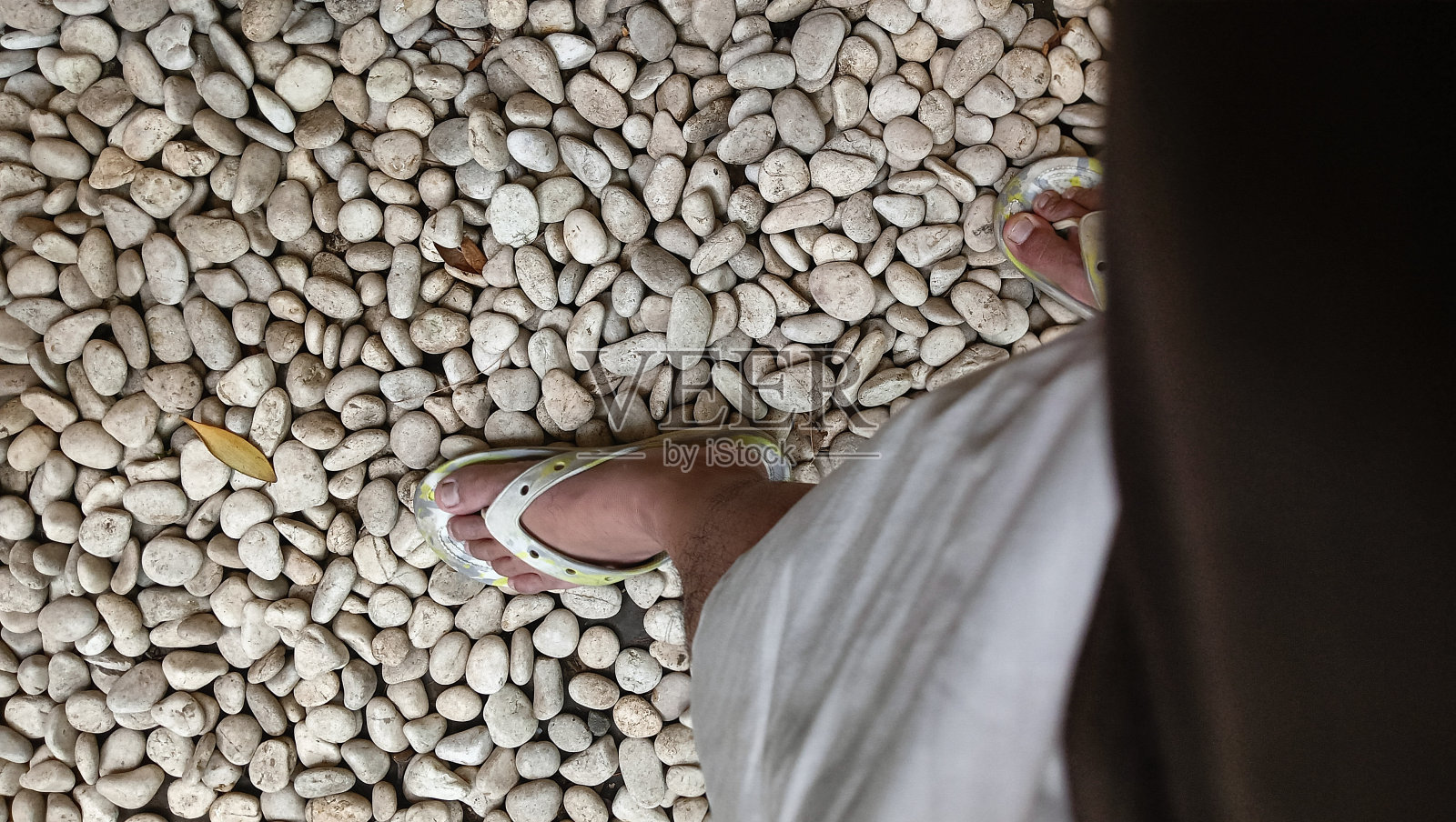 男人的脚穿着凉鞋走在白色的鹅卵石。前视图。副本的空间。照片摄影图片