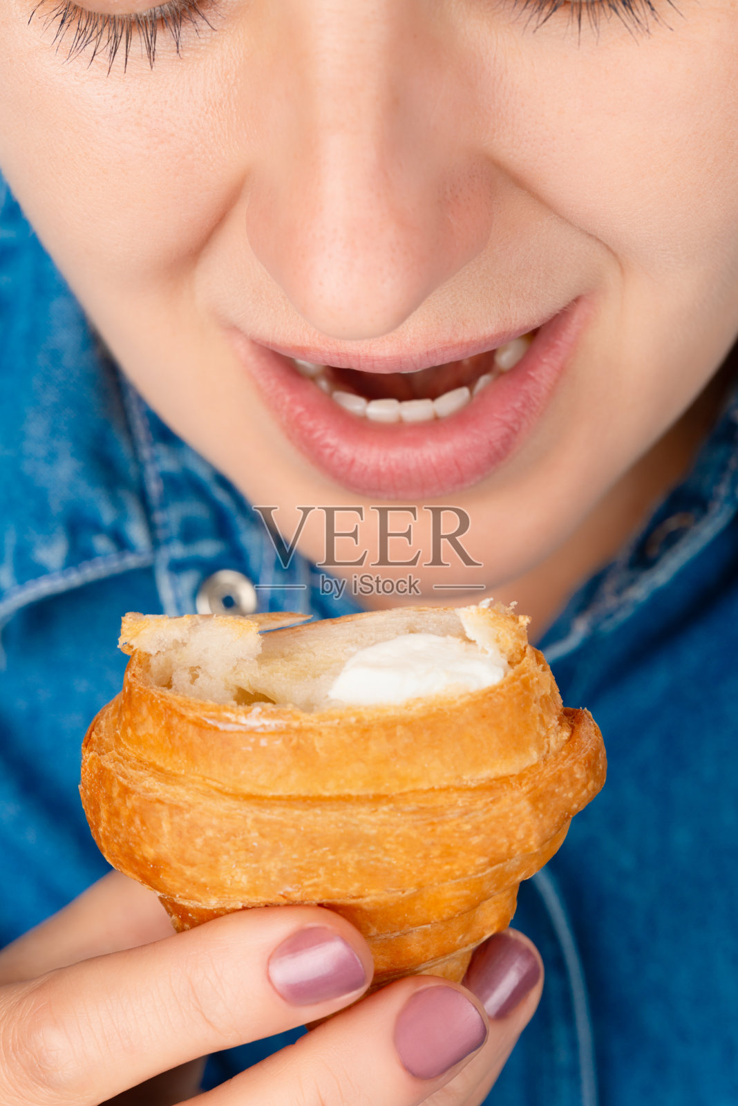 一个漂亮的白人女人的特写，她张着嘴，面前拿着一个咬过的羊角面包。从高角度看前面。垂直的框架。照片摄影图片