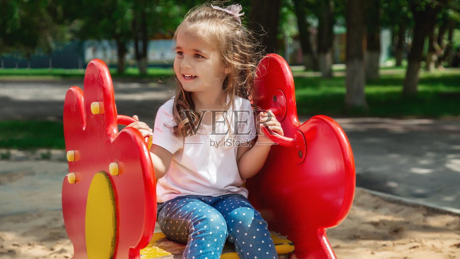 一个可爱的小女孩正在孩子们的院子里玩耍。为孩子们提供健康的夏季乐趣。小女孩在操场上沿着街道爬。儿童户外游戏。照片摄影图片