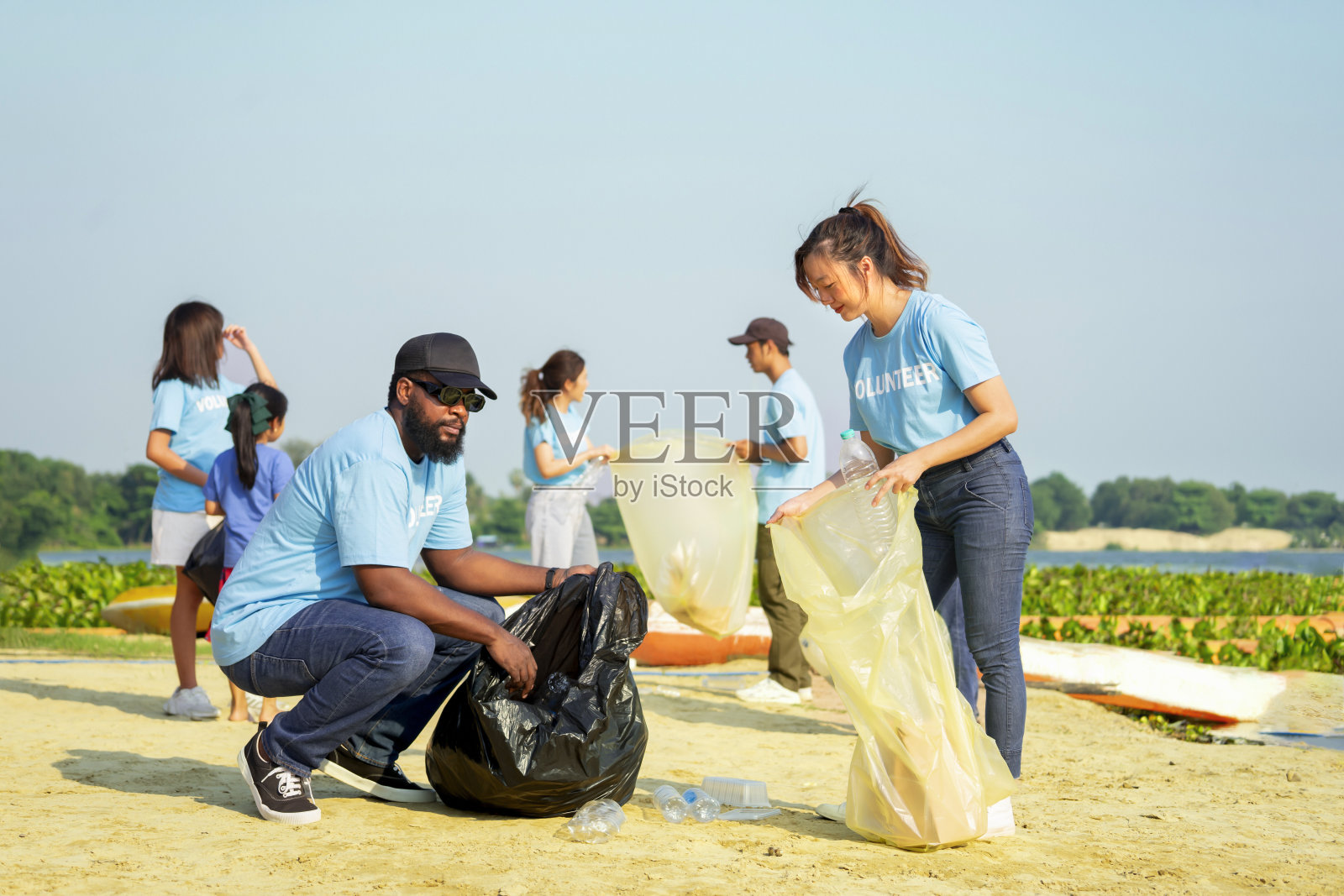 一群不同的志愿者聚集在一起清理沙滩，收集垃圾，分类垃圾照片摄影图片