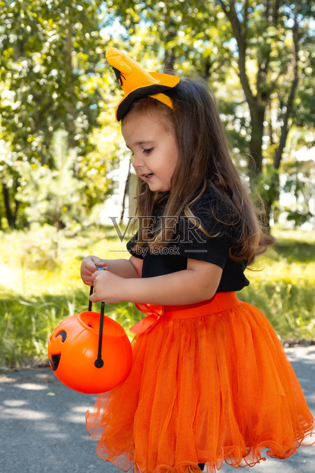 穿着女巫服装的可爱小女孩在外面举着南瓜杰克灯笼。万圣节的庆祝活动。照片摄影图片