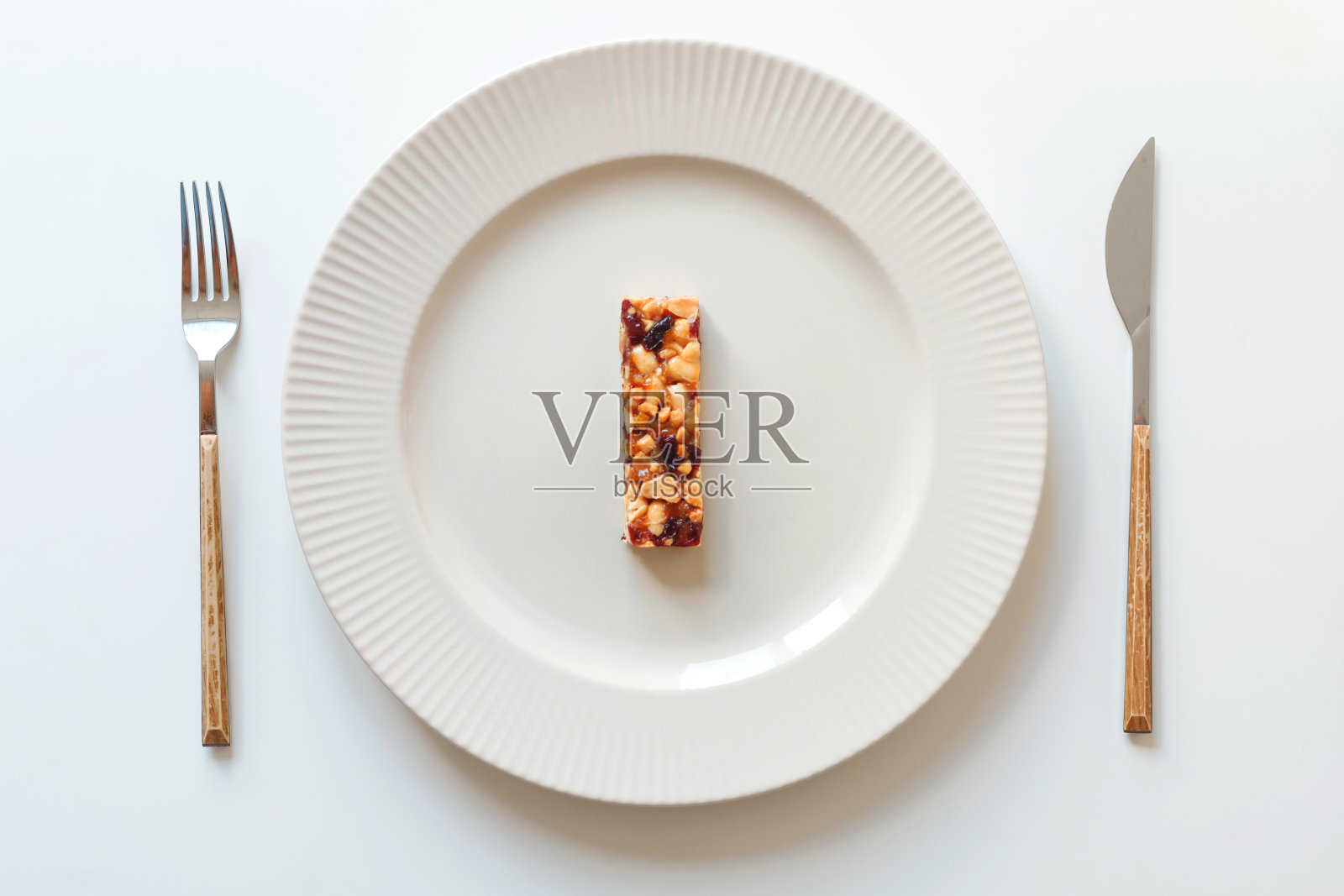 盘子里有一根什锦麦片棒。刀叉放在白色上。能量谷物食品，饮食理念照片摄影图片