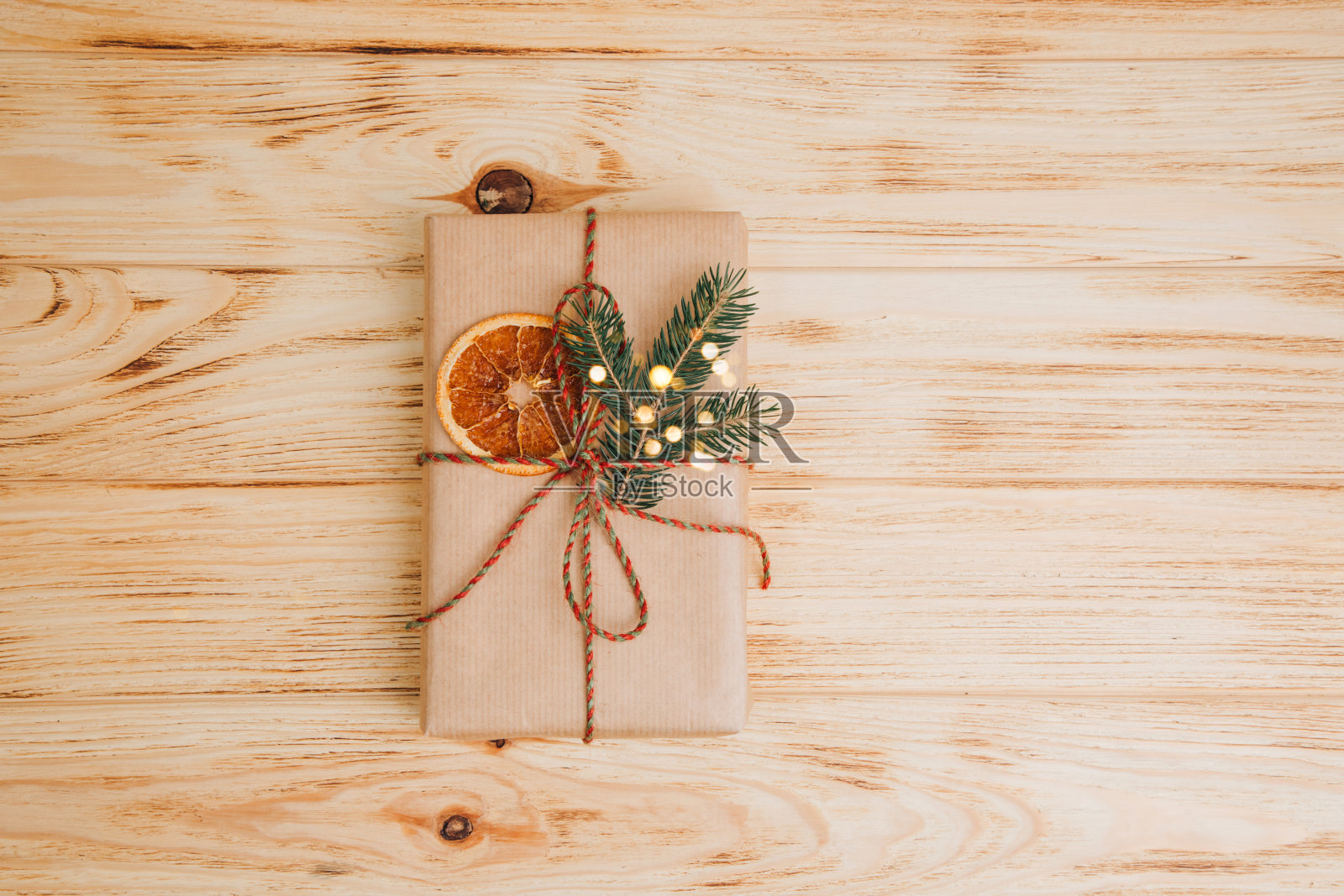 问候的背景。礼品包装在棕色的纸与干橙和针叶树的树枝在一个轻的木制背景照片摄影图片