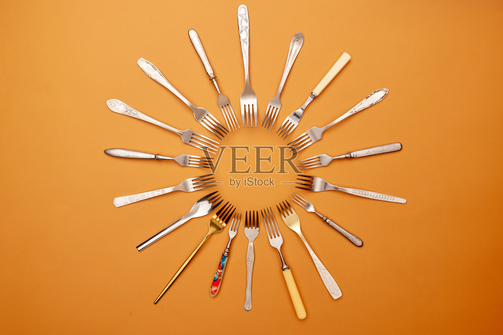 餐具。波普艺术风格。各种不锈钢，古董银器和金叉布置在橙色工作室背景的圆形平面。照片摄影图片