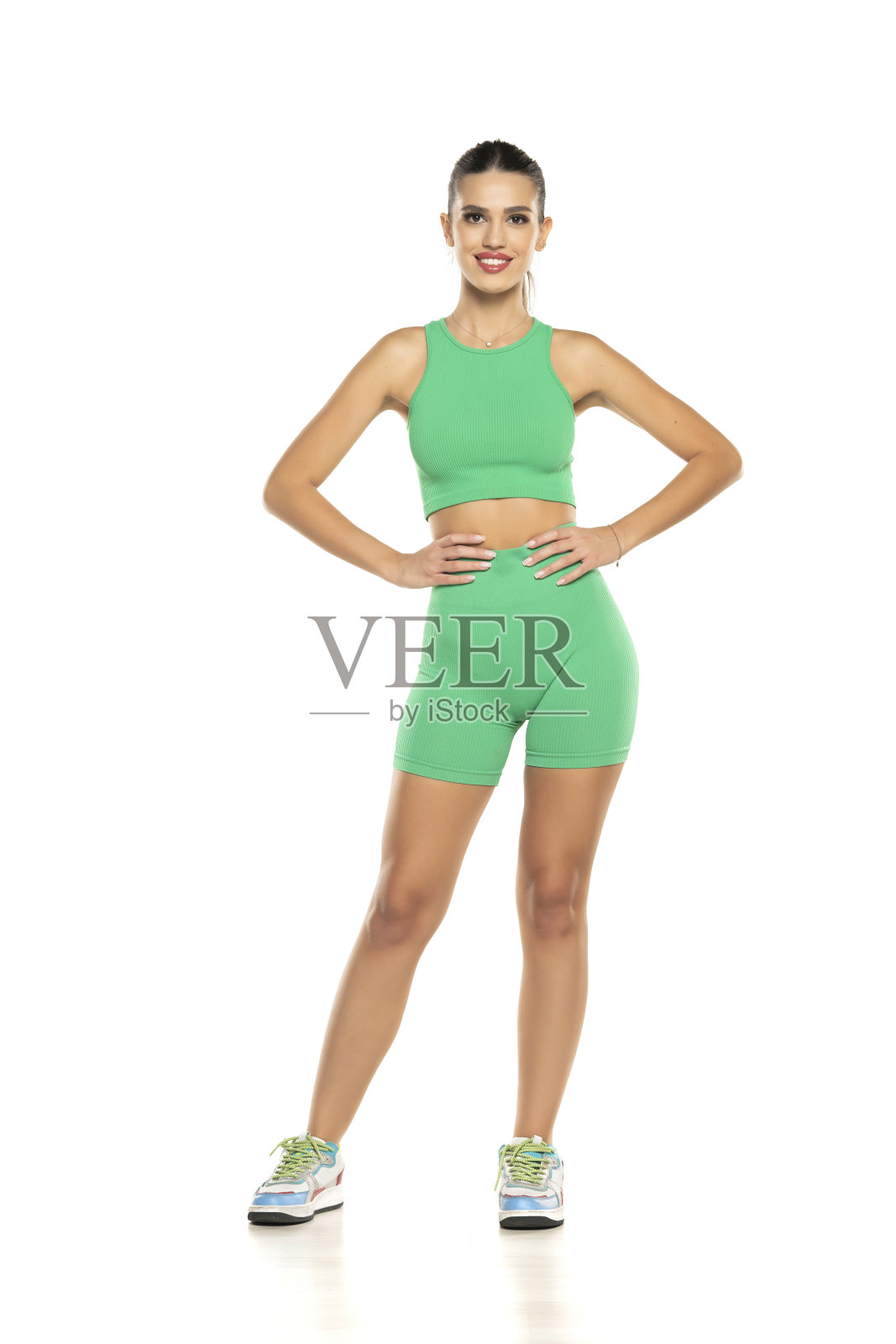 穿着绿色短裤和上衣的年轻运动微笑女子在白色背景上摆姿势照片摄影图片