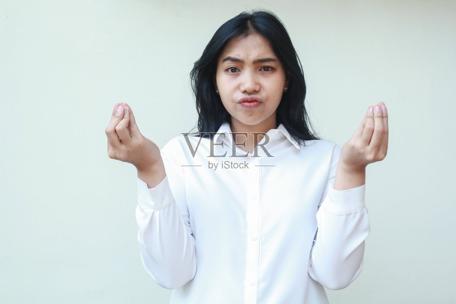 困惑的亚洲年轻商业女经理的肖像，看着镜头，举起手臂，卷起手指，穿着白色的正装衬衫，站着质疑，做出难以置信的姿态照片摄影图片